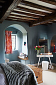 Beamed celing and arched window with blue painted walls in bedroom of Northumbrian manor house England UK