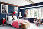 Modern armchair with white metal framed double bed in dark blue bedroom of Northumbrian manor house England UK