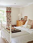 White metal bed with folded blankets and floral curtains in Northumbrian home England UK