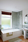 Frosted glass window above grey tiled bath and shower fitting in Birmingham home England UK