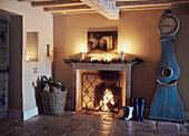 Boots and firewood with grandfather clock by lit fire in Oxfordshire home