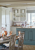 Light blue fitted units below glass fronted wall shelving in Oxfordshire kitchen England UK