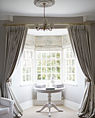 Books on pedestal base table in bay window with room divider in County Durham home England UK
