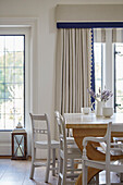 White painted chairs at wooden table in dining room of modernised Northumbrian country house UK