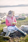 Mädchen sitzt auf einem Felsen am Strand und isst Lachs-Baguette in der Grafschaft Sligo Connacht Irland