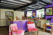 Mismatched chairs under beamed ceiling in purple and beige kitchen 18th century Northumbrian mill house, UK