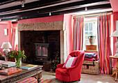 Red armchair with carved wooden coffee table at fireside in pink living room of 18th century Northumbrian mill house, UK