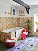 Beige tiled bath surround with pink stool and basket in18th century Northumbrian mill house, UK