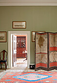 Antique folding screen and patterned rug with view through doorway in Capheaton Hall, Northumberland, UK