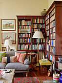 Standard lamps and bookcase with grey sofa in living room Capheaton Hall, Northumberland, UK