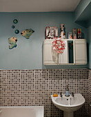 Fish ornament and cabinet above washbasin in mosaic tiled bathroom in County Durham home, North East England, UK