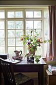 Cut flowers on wooden desk at window in Powys cottage, Wales, UK