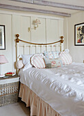 Cushions on brass bed with bedside table in panelled Warwickshire farmhouse bedroom, UK