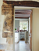 Exposed stone wall detail with view through doorway to beamed kitchen in Oxfordshire home, UK