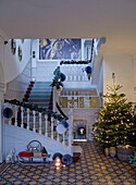 Garlands on banister with Christmas tree and sledge in spacious tiled entrance hall of East Grinstead home, West Sussex, UK