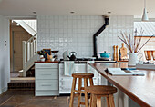 Wooden bar stools at breakfast bar in white tiled kitchen of Worcestershire home, England, UK