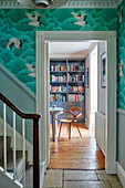 1940s wooden armchair and bookcase viewed through modernised hallway in Regency home, Cotswolds, England, UK