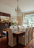 Slip-covered dining chairs with lit candles and polished wooden floor in, UK home