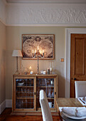 Wall map and lit candles above glass fronted display cabinet in dining room of, UK home