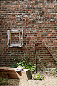 Empty picture frame with sunhat on wooden bench outside brick barn conversion, Rye, East Sussex