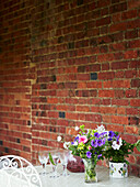 Schnittblumen und Wassergläser auf einem Tisch mit Backsteinmauer in Syresham, Northamptonshire, UK