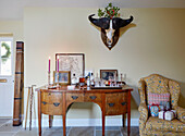 Christmas presents on armchair with wooden sideboard and animal horns in Northumberland farmhouse, UK