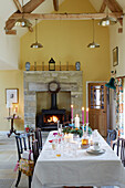 Dining table and lit woodburning stove in double height Northumberland farmhouse, UK