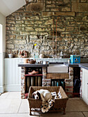Wellington boots and sink with exposed stone wall in entrance room of Northumberland farmhouse, UK