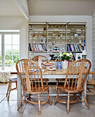 Wooden dining table and chairs iwith books on shelving in Northumberland farmhouse, UK