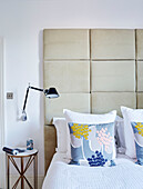 Oversized suede headboard with lamp beside double bed in South East London home, UK
