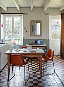 Stühle im Retrostil am Holztisch in der Küche eines bretonischen Landhauses mit gefliestem Boden in Frankreich