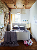 Paper shades above double bed with exposed stone wall in Brittany cottage, France
