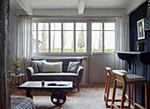 Gret sofa below window with salvaged trolley as coffee table Brittany cottage, France