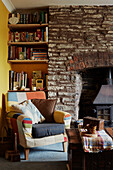 Bookshelves and armchair at exposed stone fireside in Gladestry cottage on South Wales borders