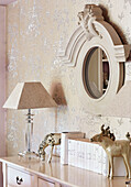 Circular mirror and lamp with ornaments on sideboard in Cotswolds cottage, UK