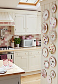 decorative plates with pink kitchenware in white fitted Cotswolds kitchen, UK