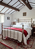Silver metal framed bed with red blanket and beamed ceiling in renovated Yorkshire farmhouse, UK
