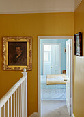 Vergoldetes gerahmtes Porträt in gelbem Flur mit Blick durch die Tür zu einem hellblauen Schlafzimmer in einem Haus im Norden, UK