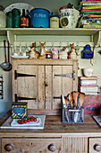 Kitchenware and ornaments with books on shelf above wooden worktop in Somerset, UK