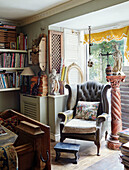 Grey buttoned armchair and plinth with bookshelves in Somerset home, UK