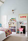 LOVE' print and bookcase with patchwork quilt in girl's room of Oxfordshire home, UK
