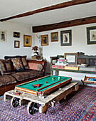 Small pool table on casters with brown leather sofa and embroidered cushions in North Yorkshire farmhouse, UK