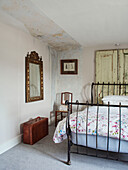 Gilt framed mirror and suitcase with metal framed bed in North Yorkshire farmhouse, UK