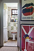 Framed prints in hallway with view to papered bathroom in Oxfordshire farmhouse, UK