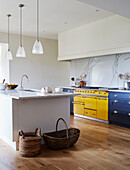 Wicker baskets on wooden floor in spacious kitchen with yellow oven in North Yorkshire farmhouse, UK