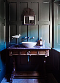 Vogel-Ornament und Waschbecken auf antikem Holz-Waschtisch in getäfeltem Badezimmer mit Spiegel in einem Bauernhaus in North Yorkshire, UK