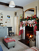 Weihnachtsstrümpfe hängen über Kamin mit Feuer und Spiege, davor Fußhocker in einem britischen Haus
