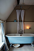 Turquoise clawfoot bath with shower rail at window in, UK cottage
