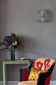 Colourful chair with flowers on leather side table and glass wall sconce in London apartment, UK