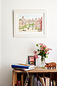 Framed artwork above bookcase with notebooks and cut honeysuckle in, UK cottage